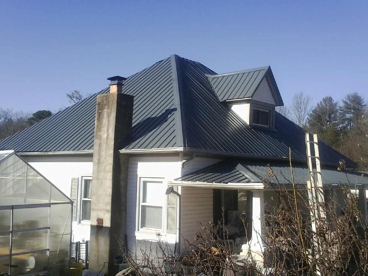 Dark blue standing seam metal roof on a white farmhouse with dormer — Slate & Tile Roof Repair by Roofing Brothers in Rumson