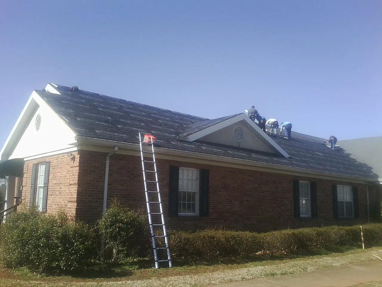 Crew tearing shingles off a brick ranch roof with a ladder set — Emergency Roof Repair work by our crew in Rumson