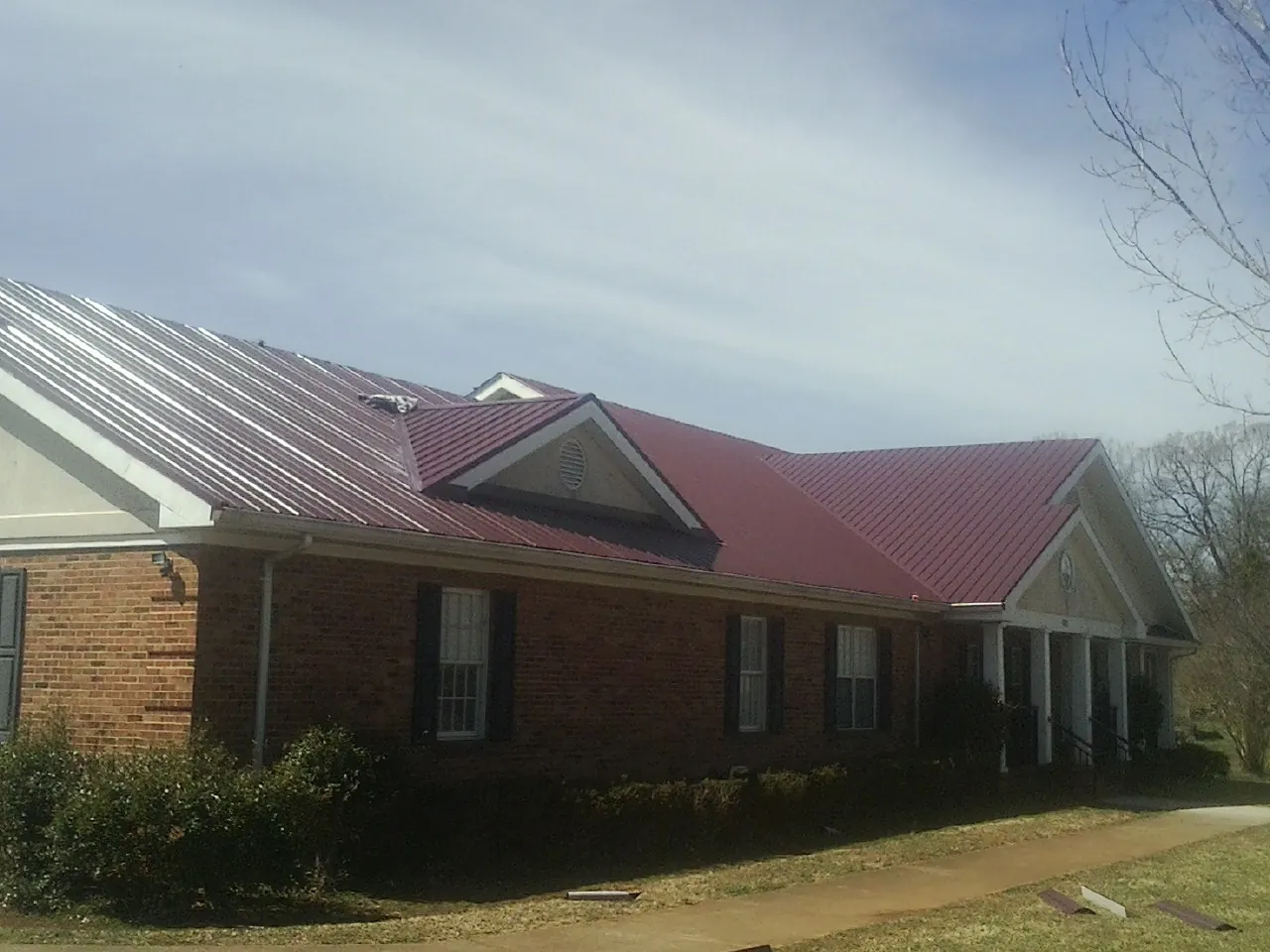 Red metal roof with gabled entries on a long brick building, from a Hail Damage Roof Repair job in Rumson