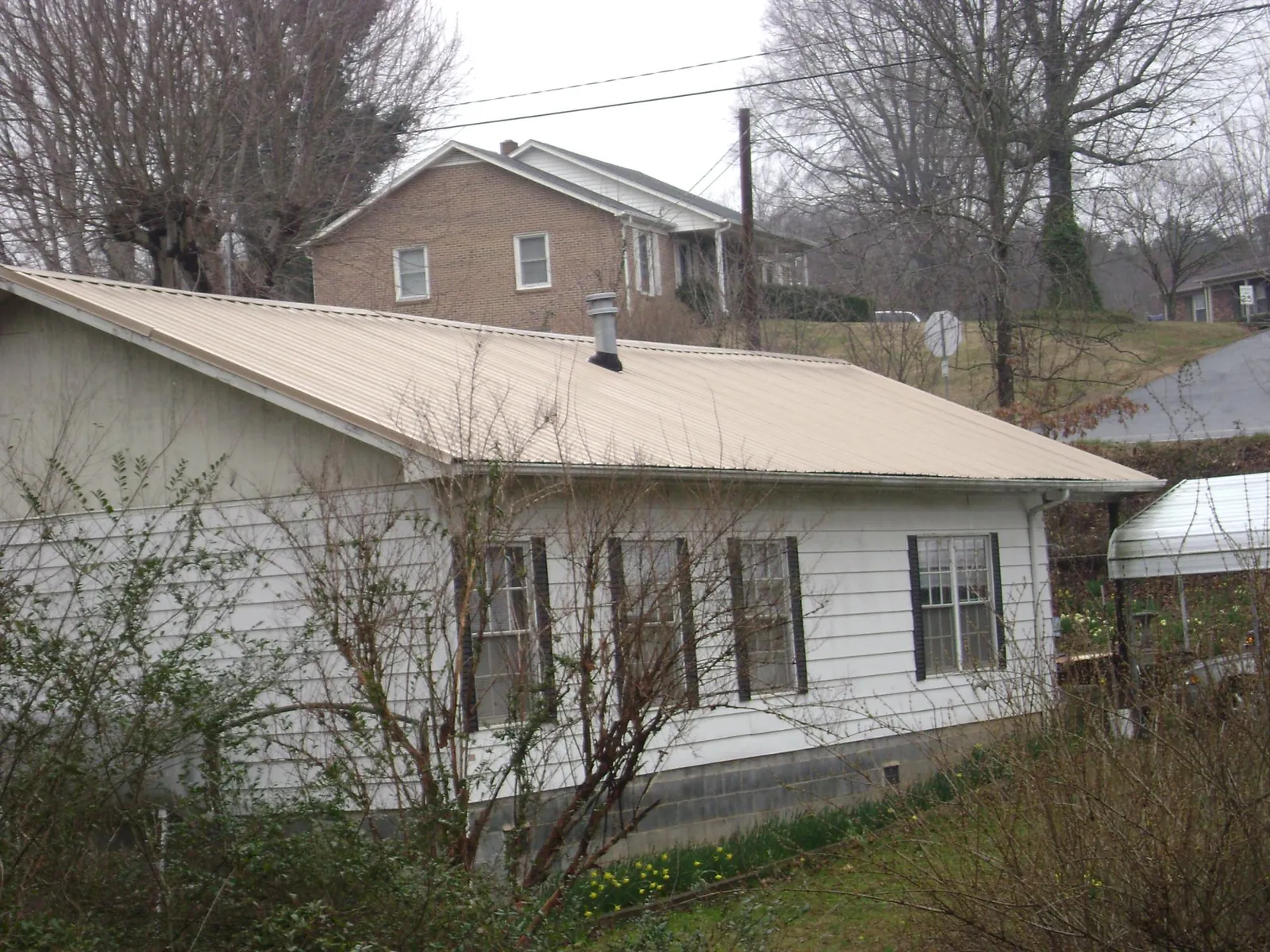 Tan metal roof on a white sided house set into a hillside — Commercial Roofing by Roofing Brothers in Rumson